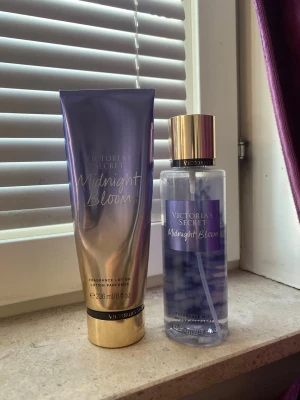 Victoria's Secret Midnight Bloom set - Säljer ett set med Victoria's Secret Midnight Bloom, innehållande en body mist och en matchande lotion. Flaskan och tuben har en snygg lila och guldig design med metallic-detaljer. Perfekt för dig som gillar blommiga och fräscha dofter.