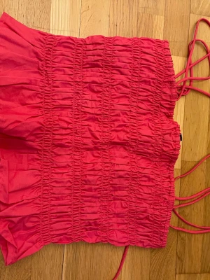 Röd smockad linne från H&M Divided - Snygg rött linne från H&M Divided smockad och tunna axelband. Kort modell med luftig passform, perfekt för sommardagar. Tillverkad i mjukt tyg som känns skönt mot huden.