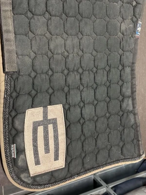 Svart schabrak från Equiline - Säljer ett svart schabrak från Equiline med quiltat mönster och beige kant. Stor beige logga på ena sidan. Perfekt för dig som vill ha en snygg och stilren look till hästen.