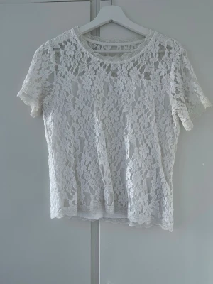 Vit spetsblus från Cream - Säljer en superfin vit spetsblus från Cream. Blusen har korta ärmar och är helt täckt av blommig spets med rund halsringning. Perfekt att styla med jeans eller kjol för en fräsch look. Blusen är lätt och luftig, vilket gör den skön att bära under varma dagar.