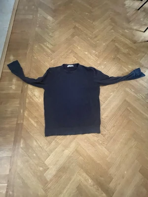 Mörkblå stickad tröja Stone Island - Mörkblå stickad tröja från Stone Island med rund halsringning och långa ärmar. Tröjan har en enkel och stilren design, perfekt för dig som gillar klassiska plagg med en modern touch. Materialet känns mjukt och följsamt.