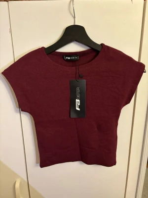 Vinröd topp från FB Sister - Snygg vinröd topp från FB Sister med rund halsringning och korta ärmar. Tillverkad i mjuk bomull som känns skön mot huden. Liten i storleken.