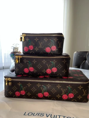 Louis Vuitton necessärer med körsbär - Säljer ett set med tre Louis Vuitton necessärer i klassiskt brunt monogrammönster med färgglada körsbärsmotiv. Väskorna har guldfärgade dragkedjor och rektangulär form. Perfekta för att organisera smink eller småprylar i väskan. Storlek S M L