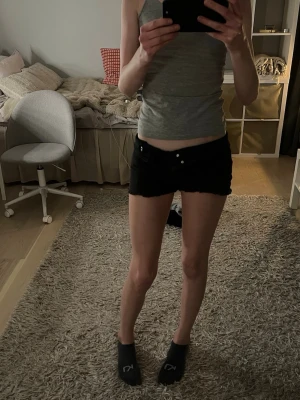 Svarta low waist shorts - Säljer ett par svarta lågmidjade shorts med knapp- och dragkedjestängning framtill. Klassisk modell med korta ben och enkel design, perfekta för varma dagar. Passar dig som gillar en basic och stilren look.