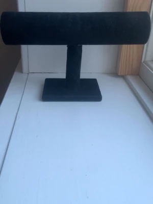 Svart smyckesställ för armband & klockor  - Säljer ett svart armbandställ, med T-formad design. Perfekt för att visa upp eller organisera armband och klockor. Stället har en stadig rektangulär fot och en rundad stång för smycken.