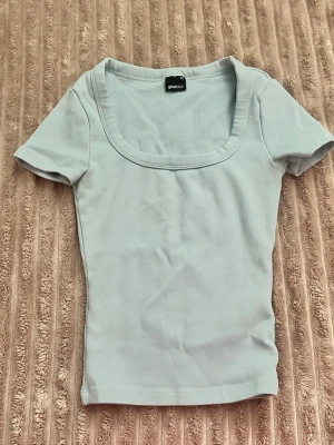 Ljusblå ribbad topp från Gina Tricot - Supersöt ljusblå topp från Gina Tricot med ribbad struktur och fyrkantig ringning. Kortärmad och figurnära passform som passar perfekt till jeans eller kjol. Enkel men ändå stylish basic som är lätt att matcha.