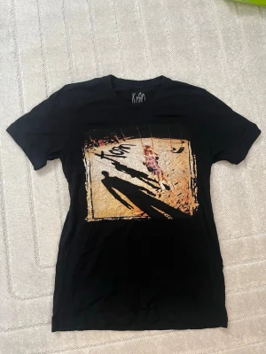 Svart Korn t-shirt med tryck - Säljer en svart t-shirt från Korn. T-shirten har rund hals och korta ärmar. Perfekt för dig som gillar bandmerch och vill sticka ut.