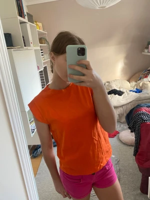 Orange topp - Snygg orange topp med enkel och rak passform. Perfekt för dig som gillar färgstarka plagg och vill sticka ut lite extra. Toppen är i ett mjukt material och passar bra till både jeans och shorts.