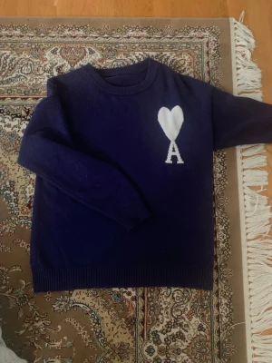Ami paris sweatshirt  - Mysig mörkblå stickad tröja med rund hals och ribbade muddar. På bröstet finns ett vitt hjärta ovanför bokstaven 'A' som ger en unik och trendig look. Perfekt för dig som gillar stilrena detaljer och vill ha något som sticker ut.