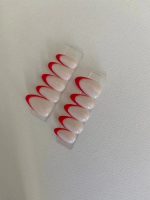 Press-on naglar med röd fransk tipp - Snygga press-on naglar i mandelform med milky bas och röd fransk tipp. Perfekt för dig som vill ha en trendig och stilren look utan att behöva gå till salong. Lätta att applicera och ta bort.