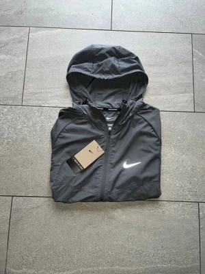 Grå nike runner vindjacka - Snygg nike runner. Färgen är grå och den har feta reflexer. Storlek S. Prislappen är kvar. Fraktar samma dag.