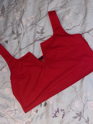 Röd topp med V-ringning - Snygg röd topp med breda axelband och djup V-ringning framtill. Toppen har en enkel och stilren design utan synliga detaljer eller spets. Perfekt för dig som vill ha en bekväm och trendig look under kläderna.