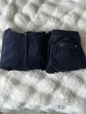 Mörkblå juicy couture set - Mörkblått juicy couture set med matchande byxor och jacka. St. 12/13 år. Bra skick, använd några gånger. Knappar på byxfickorna, resår i midjan. Köpt ny för 1800kr