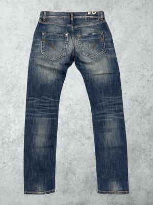Blå slitna jeans från Dondup  - Säljer ett par blå jeans från Dondup med snyggt slitna detaljer och ljusa partier framtill. Klassisk femficksmodell med raka ben och kontrastsömmar. Perfekta för en avslappnad och trendig look. Modell: SAM. Mått: Bredd; 40 cm. Längd; 102 cm.