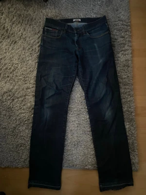 Faded jeans från Tommy Hilfiger  - Säljer ett par klassiska mörkblå jeans från tommy Hilfiger med raka ben och fetta fades . Jeansen har kontrastsömmar och en fett snus fade på bakfickan. Perfekta till en avslappnad stil och funkar året runt.