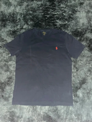 Ralph lauren t-shirt (M)Ralph lauren t-shirt (M) - Stilren Ralph Lauren T-shirt i marinblå färg, storlek M. Bra skick, använd men väl omhändertagen. Perfekt för både casual och mer uppklädda outfits. Klassisk design med hög kvalitet som håller länge.  Detaljer: 	•	Storlek: M 	•	Färg: Marinblå 	•	Material: 100% bomull (bekväm och mjuk) 	•	Skick: Bra