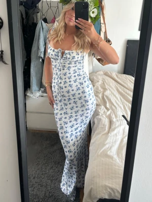 Vit långklänning med blå blommor - Supersöt långklänning i vitt med blått blommönster och smala axelband. Perfekt för sommarens alla tillfällen! Använd en gång på midsommar för några år sedan .