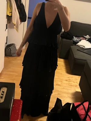 Marinblå långklänning med volanger - Elegant marinblå långklänning med djup v-ringning och flera lager av plisserade volanger. Klänningen är ärmlös och har en flytande, luftig passform som ger en sofistikerad look. Perfekt till balen🥰 skriv för prisförslag eller fler bilder