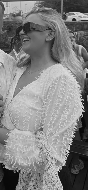 Vit blus med struktur från Gina Tricot - Trendig vit blus från Gina Tricot med v-ringning och långärmade puffärmar. Blusen har ett unikt strukturerat tyg med dekorativa fransar och spetsdetaljer vid ärmsluten. Perfekt för dig som vill sticka ut med en cool och modern look.