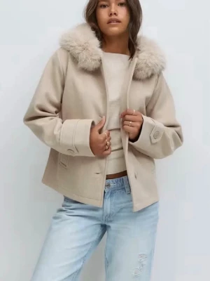 Beige kappa med fuskpäls - Stilren beige kappa med stor krage i fuskpäls. Kortare modell med raka ärmar och knappar framtill. Perfekt för dig som gillar en trendig och mysig look. Passar till både jeans och kjol. Materialet ser ut att vara ullblandning.