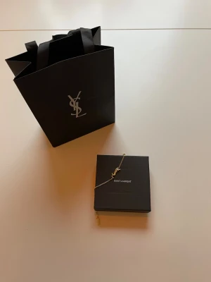 Guldigt armband från Yves Saint Laurent - Säljer ett armband från Yves Saint Laurent den är helt guld färgad. Det som kommer med de är original lådan som man också kan sätta smycken i och original påsen kommer också med. Säljer den för 800kr, skicka paketet samma dag eller dagen efter ☺️