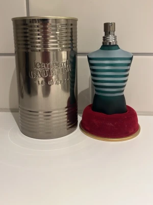 Jean Paul Gaultier Le Male 75ml - Jean Paul Gaultier Le Male parfym i den ikoniska flaskan formad som en manlig torso med blå och turkosa ränder. Kommer med original metallburk och röd sammetsbas. En klassisk doft som sticker ut både i design och doft.