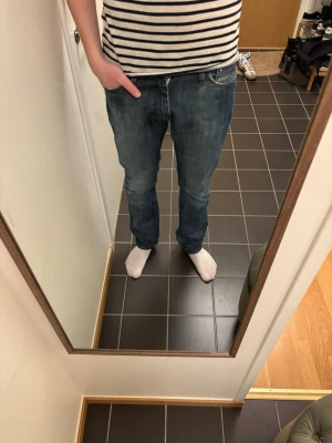 Blå raka jeans från Acne Jeans - Säljer ett par klassiska blå jeans från Acne med rak passform och fem fickor. Jeansen har snygga slitningar och kontrastsömmar, tillverkade i bomull med lite stretch för extra komfort. Perfekta till en avslappnad stil.