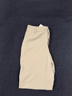 Grå golf byxor från J.Lindeberg - Säljer ett par Grå golfbyxor från J.Lindeberg. Byxorna har elastisk midja, bälteshällor och är tillverkade i ett lätt, rutmönstrat funktionsmaterial som andas. Perfekta för träning eller utomhusaktiviteter.