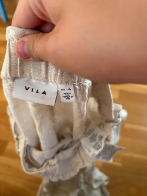 Beiga leggings från VILA, strl 36 - Säljer ett par beiga linne byxor från VILA i storlek 36. De har resår i midjan och är tillverkade i ett mjukt, tunt material som känns skönt mot huden. Perfekta för en avslappnad och chill stil.  OBS EN FLÄCK VID BENEN!!
