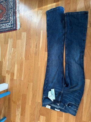 Blå bootcut jeans från Gina -  Aldrig använda. Tagen är kvar. Säljer ett par blå bootcut jeans från Gina tricot med låg midja. Klassisk femficksmodell i stretchigt denimtyg. Snygg tvättad look och raka, utsvängda ben. Perfekta till sneakers eller boots.
