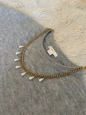 Guldhalsband med droppformade pärlor - Snyggt halsband  i guldfärgad rostfritt med droppformade vita pärlor som hänger längs kedjan. Perfekt för att ge din outfit en elegant touch. Kedjan har en klassisk design och pärlorna ger en cool kontrast.