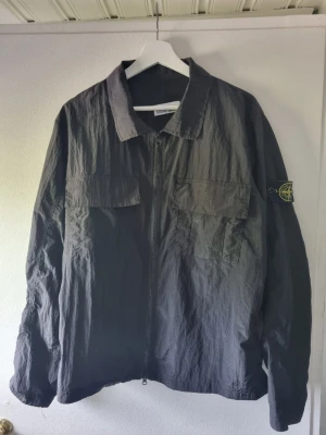 Svart overshirt från Stone Island - Säljer en svart overshirt från Stone Island med dragkedja framtill, två bröstfickor och klassisk krage. Tillverkad i ett lätt, strukturerat material