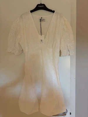 Vit kort klänning med puffärm från meet me there  - Söt vit kort klänning från KappAhl med broderade detaljer och v-ringning. Klänningen har puffiga korta ärmar och är tillverkad i bomull, vilket ger en luftig och somrig känsla. Perfekt för varma dagar och stilrena outfits.