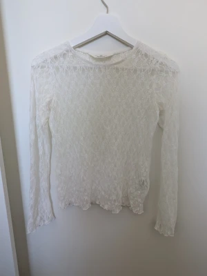 Vit spetsblus med lång ärm - Säljer en superfin vit spetsblus med lång ärm och transparent spetsmönster. Blusen har en rund halsringning och är tillverkad i ett tunt, mjukt material som ger en romantisk vibe. Perfekt att styla lager på lager eller som statement-plagg. Den är i ett nytt skick då jag aldrig har använt den men prislappen är borttagen. Skriv gärna om ni har några frågor 💕