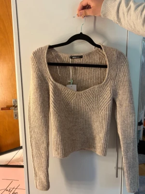 Beige stickad tröja Gina Tricot - Säljer en beige stickad tröja från Gina Tricot med ribbad struktur och snygg, djup fyrkantig ringning. Tröjan har långa ärmar och en kroppsnära passform. Perfekt att matcha med jeans eller kjol för en trendig look. Priset kan diskuteras 