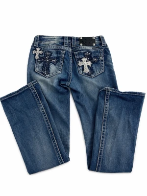 Blå Miss Me jeans med korsdetaljer - Säljer ett par blå Miss Me jeans som är Bootcut och lowwaist. Bakfickorna har snygga broderade kors med stenar och detaljer. Storlek 34/S Köpte för 2500kr och säljer nu för 899kr. Älskar dessa jeans men tyvär så kommer dom aldrig till användning. Byxknappen har ramlat av men det är bara att sätta dit en ny eller vara utan. För mig har det funkar bra utan Byxknapp. Lite slitningar i byxbenen annars inget fel på dom!(det går att pruta och skriv för frågor)❤️