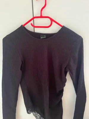 Svart långärmad topp med spets - Säljer en svart långärmad topp från Gina Tricot. Toppen har en ribbad struktur och en snygg spetsdetalj längst ner. Perfekt att styla med jeans eller kjol för en trendig look.