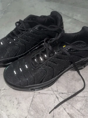 Svarta sneakers med reflekterande detaljer - Snygga svarta sneakers med mesh och syntetpaneler, samt reflekterande detaljer på ovandelen. Skorna har en sportig siluett, svarta skosnören och en robust sula. Perfekta för dig som gillar en clean och modern look.
