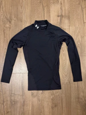 HeatGear Armour Långärmad Kompressionströja Svart - Denna långärmade träningströja är skapad i Under Armours egna HeatGear®-tyg som har alla fördelar av deras klassiska kompressionsplagg men med en ännu lättare känsla. Materialet hjälper dig prestera på topp och samtidigt hålla dig bekväm under hela träningspasset.  HeatGear®-material Kompression Lätt och luftig känsla Snabbtorkande och svettresistent Hög krage