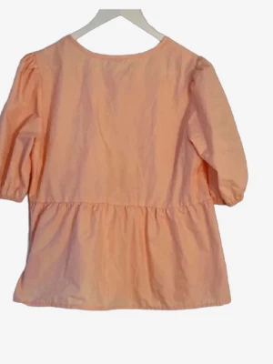 Persikofärgad blus med puffärm och knyt🌸 - Söt persikofärgad blus med trekvartsärm och puffiga axlar. Blusen har en lös passform och rynkdetalj i midjan som ger en avslappnad siluett. Tillverkad i ett lätt bomullsliknande material, perfekt för en trendig vardagslook. Den har fint knyt på baksidan!