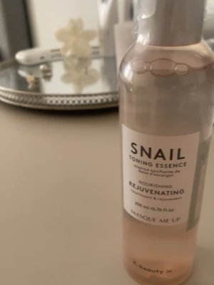 Snail Toning Essence från Masque Me Up - Snail Toning Essence från Masque Me Up är en närande och återfuktande toner med snigelextrakt. Kommer i en genomskinlig plastflaska med vitt lock och rymmer 200 ml. Vätskan är ljusrosa och flaskan har en stilren etikett med svart text. Perfekt för dig som gillar K-beauty🌸
