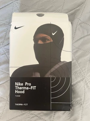 Nike Pro Therma-FIT Hood skimask - Använd 1gång för o prova annars helt ren inga hål ingen smuts ingenting helt ny. Nike Pro Therma-FIT balaclava i svart med vit Nike-logga. Tillverkad i ett stretchigt och värmande material som passar perfekt för träning utomhus. Sitter tight runt huvudet och täcker både hals och ansikte. Sportig och stilren design.