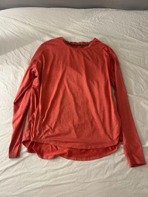 korall långärmad sporttröja H&M - Snygg korall färgad långärmad sporttröja från H&M Sport. Tillverkad i ett lätt och ventilerande funktionsmaterial som passar perfekt för träning. Tröjan har rund halsringning och något längre bakstycke för extra komfort.