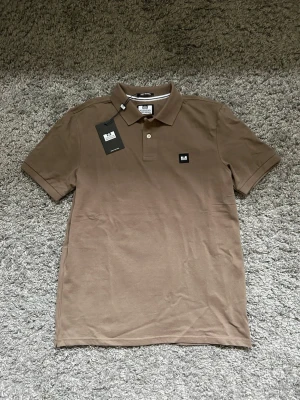 Beige pikétröja från Weekend Offender - Snygg beige pikétröja från Weekend Offender med klassisk krage och två knappar. Tröjan har en liten svartvit logotyp på bröstet och är gjord i mjuk bomull. Perfekt till jeans eller shorts för en clean och enkel stil. !SPRILLANS NY!