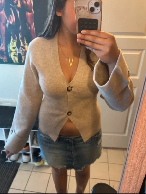 Beige fitted cardigan från Gina tricot  - Aldrig använd innan, prislappen är kvar. Säljer pga fel storlek. Snygg beige cardigan från Gina tricot med v- ringning och två stora knappar framtill. Koftan har vida ärmar med breda uppvik och en rak, något kortare passform. Perfekt att slänga över en t-shirt för en chill look.