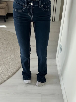 Mörkblå bootcut jeans med kontrastsömmar - Snygga mörkblå bootcut jeans från Gina Tricot med vita kontrastsömmar och dekorativa fickor bak. Jeansen har klassisk femficksmodell och är tillverkade i ett stretchigt denimtyg för skön passform.