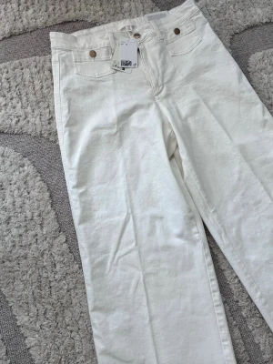 Vita raka jeans från H&M - Snygga vita jeans från H&M med raka ben och klassisk femficksmodell. Jeansen har silverfärgade knappar och är tillverkade i ett stadigt bomullstyg. Perfekta för en clean och fräsch look.