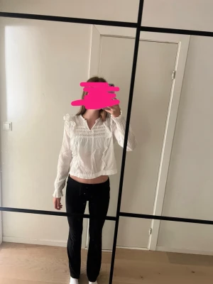 Vit kalasig blus med spetsdetaljer - Säljer en vit blus med långa ärmar och fina spetsdetaljer vid axlar och bröst. Blusen har volang vid axlarna och en lös, luftig passform. Perfekt för dig som ska på kalas.