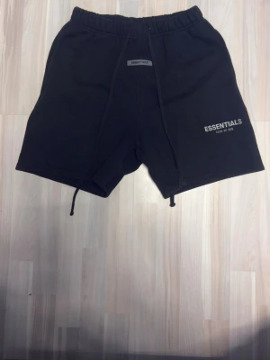 Svarta shorts från Essentials - Snygga svarta shorts från Essentials Fear of God med elastisk midja och snörning. Shortsen har en avslappnad passform och är perfekta för sommaren. Essentials-logga framtill och mjukt material för extra komfort.