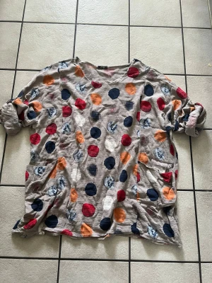 Prickig oversized topp i bomull storlek XXL - Säljer en loose och oversized topp med stora färgglada prickar i marinblått, rött, orange och vitt på en beige botten. Toppen har rund halsringning och långa ärmar som kan vikas upp. Materialet känns mjukt och luftigt, perfekt för en chill look.